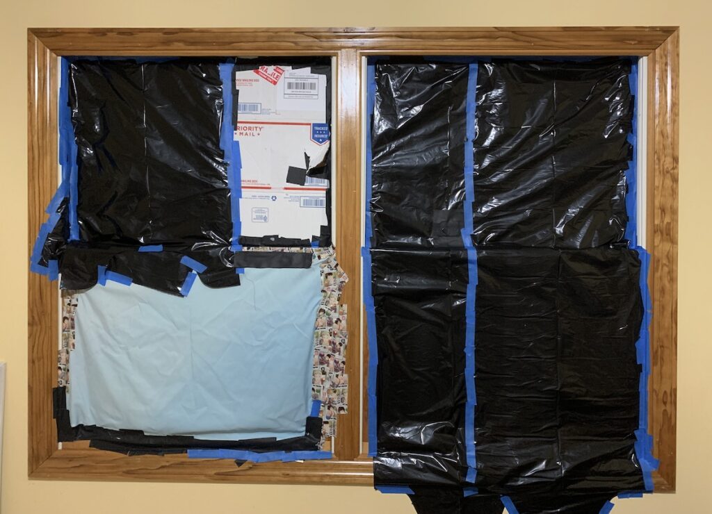 Photo of the windows in the guest room taped up with black trash bags, cardboard, black gaffer's tape, masking tape, duct tape, and a tapestry.