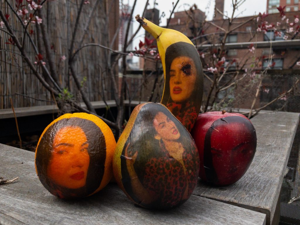 A collection of fruits arranged in a sort of still life, each one with a gel emulsion transfer of a female